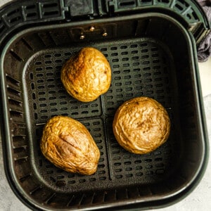 Top view of three baked potatoes in an air fryer basket