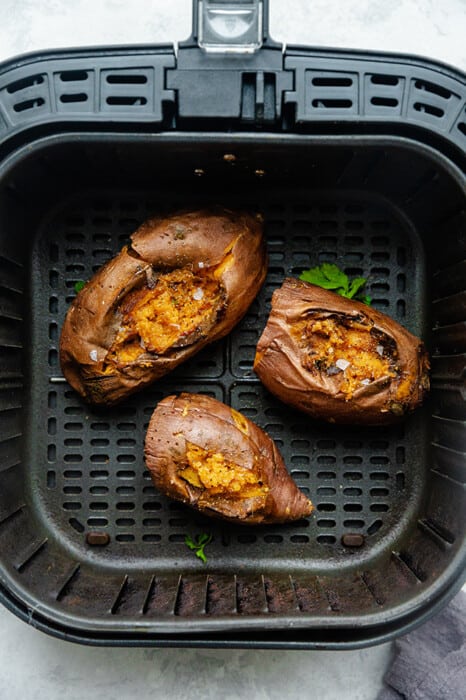 Top view of three baked sweet potatoes in an air fryer basket