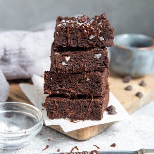 Side view of stacked fudgy paleo flourless brownies on a grey background