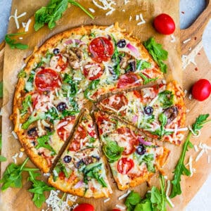 Top view of cauliflower pizza crust on parchment paper with arugula, pepperoni and tomatoes