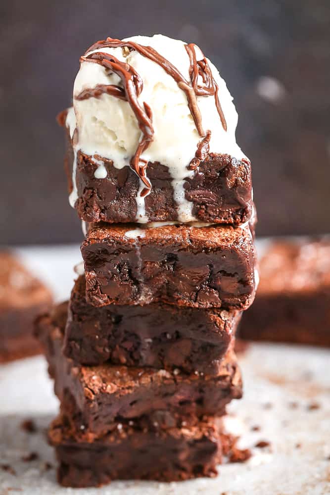 Vanilla ice cream with fudge drizzled on top of a stack of the best brownies.