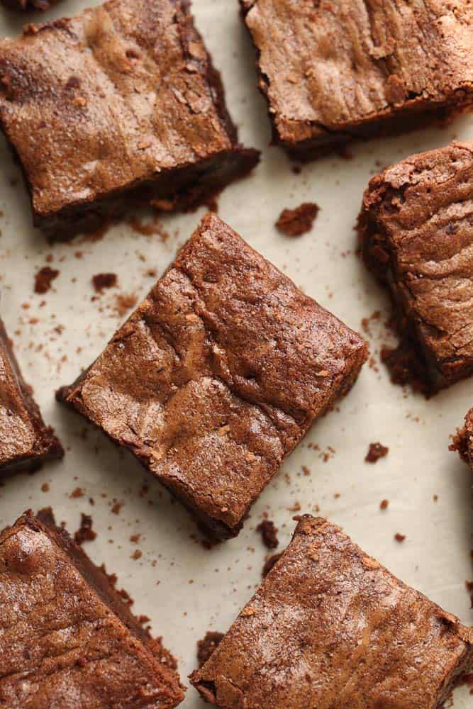 Five chocolate fudge brownies on a table surrounded by brownie crumbs.