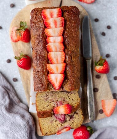 Top view of strawberry banana bread with fresh strawberries on grey surface.