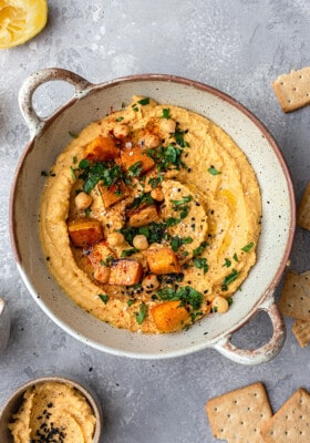 Top view of sweet potato hummus in a beige serving bowl with roasted sweet potatoes on top