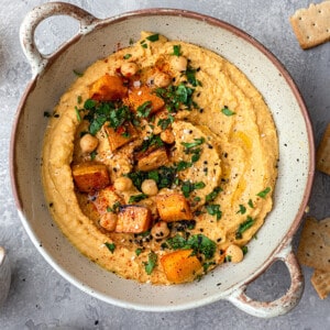Top view of sweet potato hummus in a beige serving bowl with roasted sweet potatoes on top