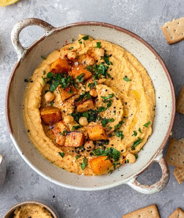 Top view of sweet potato hummus in a beige serving bowl with roasted sweet potatoes on top