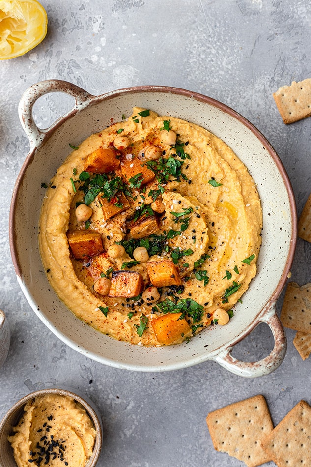 Overhead view of sweet potato hummus in a dish topped with fresh herbs, chickpeas, and sweet potato chunks