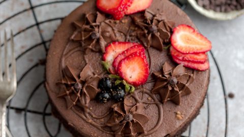 Top view of a whole keto chocolate cake on a wire rack and a grey background with strawberries and sugar free frosting