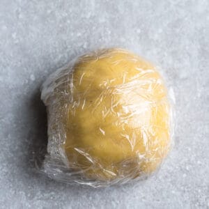 Top view of sugar cookie dough wrapped in plastic wrap on a grey background