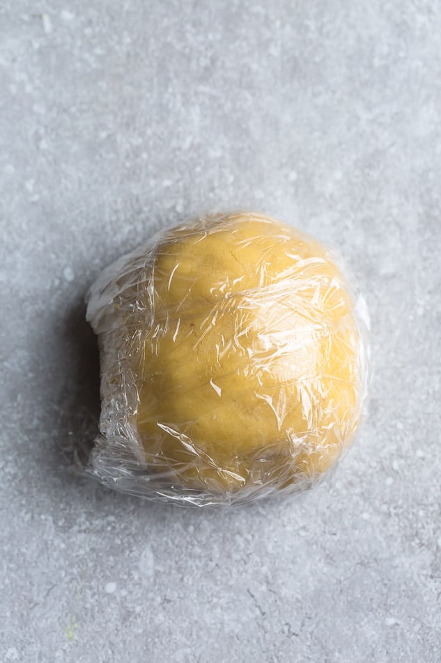 Top view of sugar cookie dough wrapped in plastic wrap on a grey background