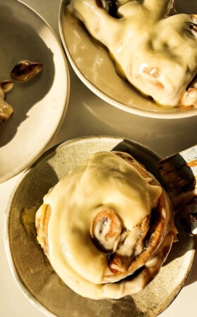 One gingerbread cinnamon roll topped with cream cheese frosting in a white bowl.