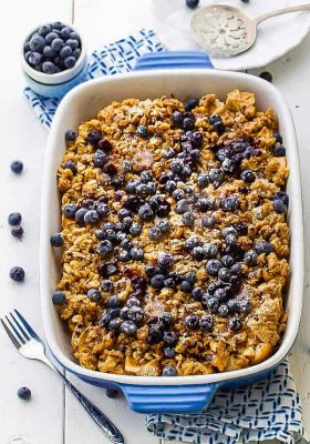 A blueberry French toast bake in a casserole dish beside a small bowl filled with fresh blueberries