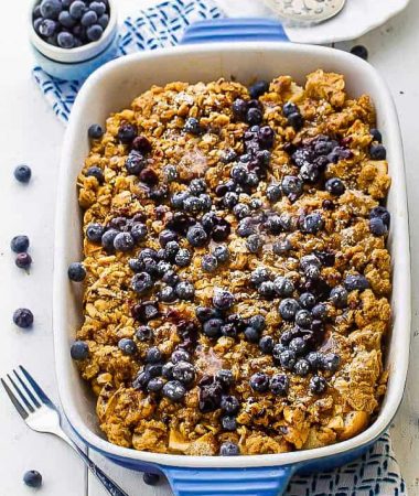 A blueberry French toast bake in a casserole dish beside a small bowl filled with fresh blueberries