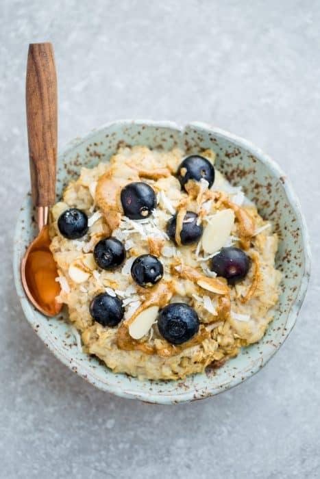A Bowl of Blueberry Oatmeal with a Wooden and Copper Spoon Inside