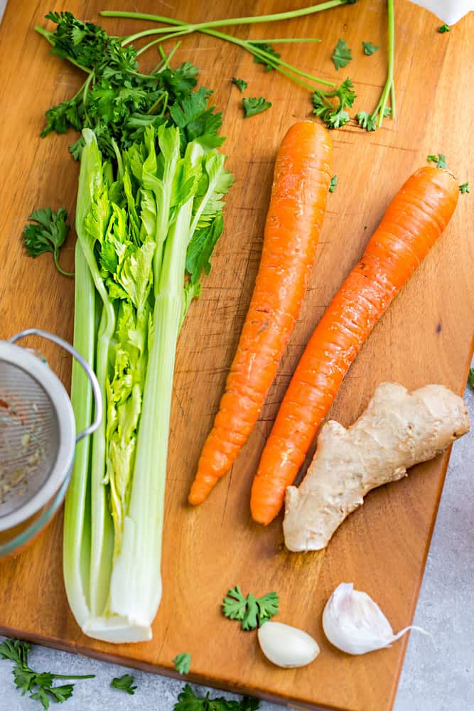 Fresh celery, ginger, carrots and garlic on a wooden cutting board.