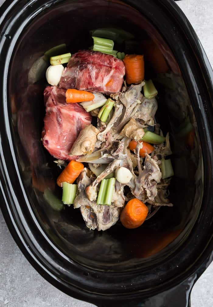 Crock pot with bone broth ingredients - celery, carrots, bones, steak and ginger.