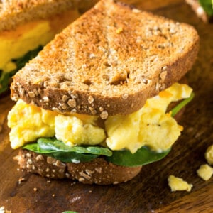A breakfast sandwich on toasted bread with scrambled eggs and baby spinach.
