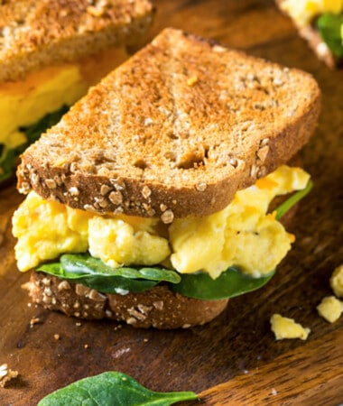 A breakfast sandwich on toasted bread with scrambled eggs and baby spinach.