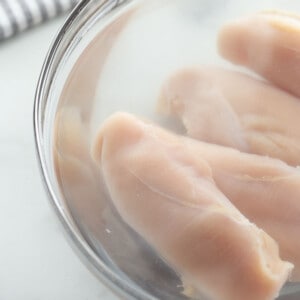 Four raw chicken breasts in a brine large clear mixing bowl