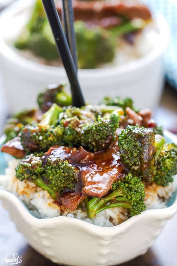 Top view of beef and broccoli stir fry in a white bowl over Jasmine rice with black chopsticks sticking up from the bowl