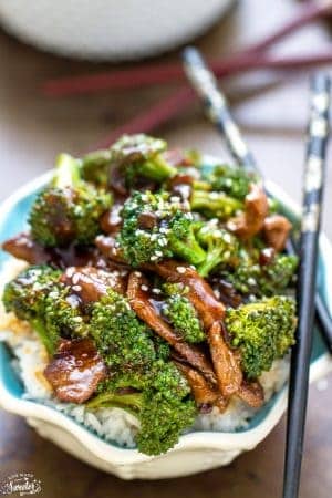 Top view of beef and broccoli stir fry in a white bowl over Jasmine rice with black chopsticks