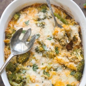 Top view of broccoli casserole with cheese in a white oval casserole dish with a stainless steel serving spoon