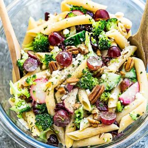 Top view of gluten free Broccoli Pasta Salad with grapes and pecans in a glass bowl with wooden spoons