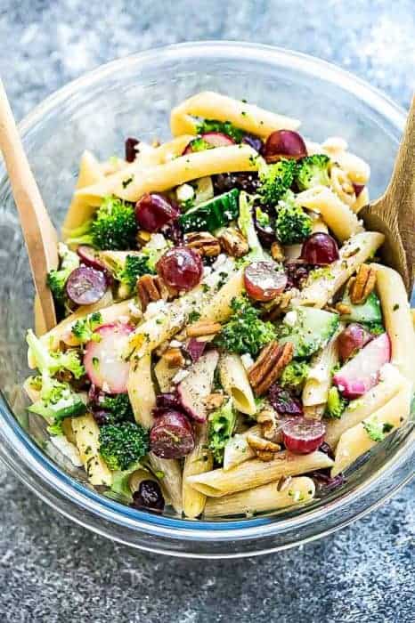 Top view of gluten free Broccoli Pasta Salad with grapes and pecans in a glass bowl with wooden spoons