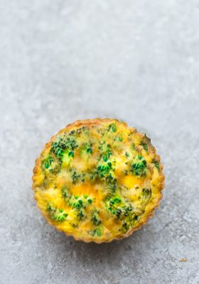 Top view of one broccoli egg muffin on a grey background