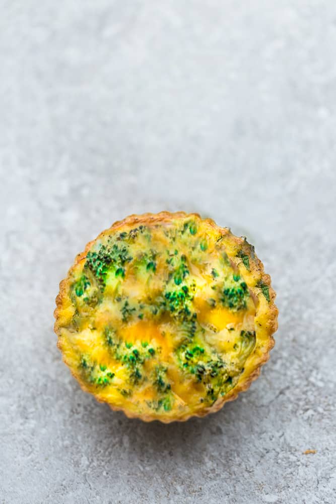 Top view of one broccoli egg muffin with cheese on a grey background