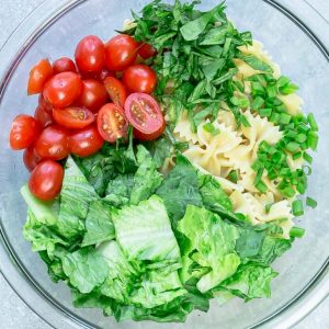 Ingredients for chicken Caesar pasta salad in glass bowl.