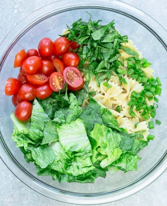 Ingredients for chicken Caesar pasta salad in glass bowl.