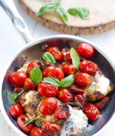 Overhead view of Caprese Chicken in a skillet topped with melted cheese, blistered tomatoes, and fresh basil
