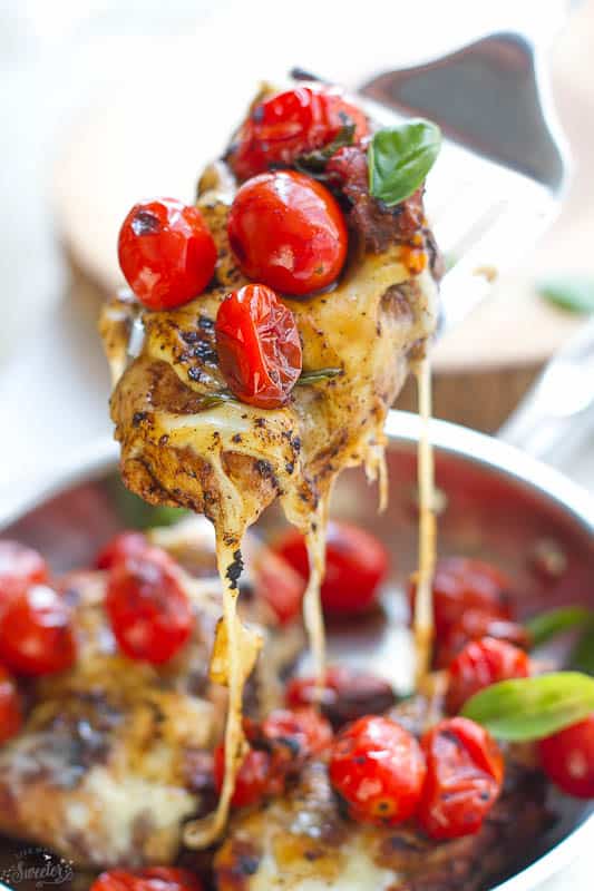 A bite of Caprese Chicken on a fork with melted cheese, blistered tomatoes, and fresh basil