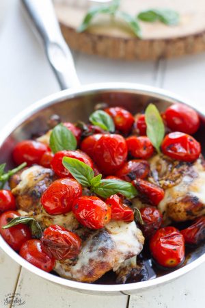 Caprese Chicken in a skillet topped with blistered tomatoes, melted cheese, and fresh basil