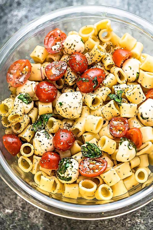 Top view of caprese pasta salad in glass bowl on grey surface.