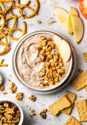 Flat lay of one apple dip in a white bowl surrounded by pretzels, apples and crackers