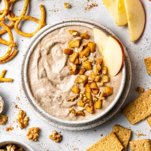 Flat lay of one apple dip in a white bowl surrounded by pretzels, apples and crackers