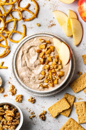 Flat lay of one apple dip in a white bowl surrounded by pretzels, apples and crackers