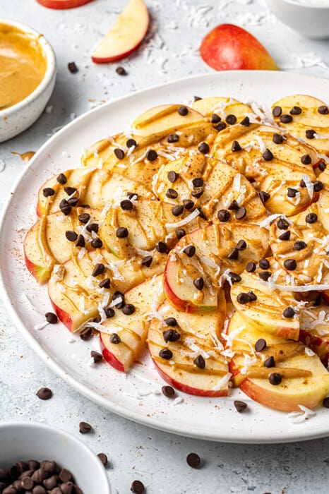 Apple slices on a plate topped with nut butter, chocolate chips, and shredded coconut