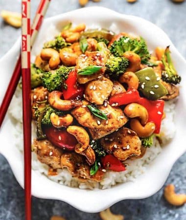 Easy Cashew Chicken on a bed of white rice in a white bowl with red chopsticks.