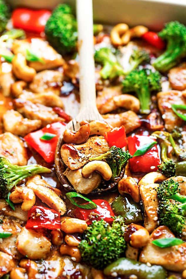 Close-up view of wooden spoon scooping Cashew Chicken and vegetables from a sheet pan