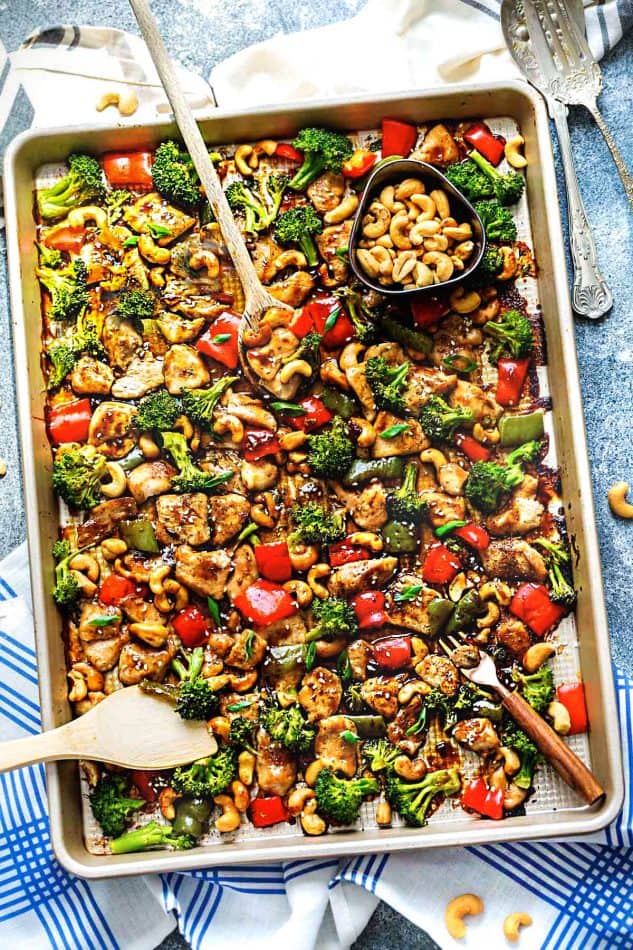 Top view of a sheet pan of Cashew Chicken with vegetables and two wooden spoons