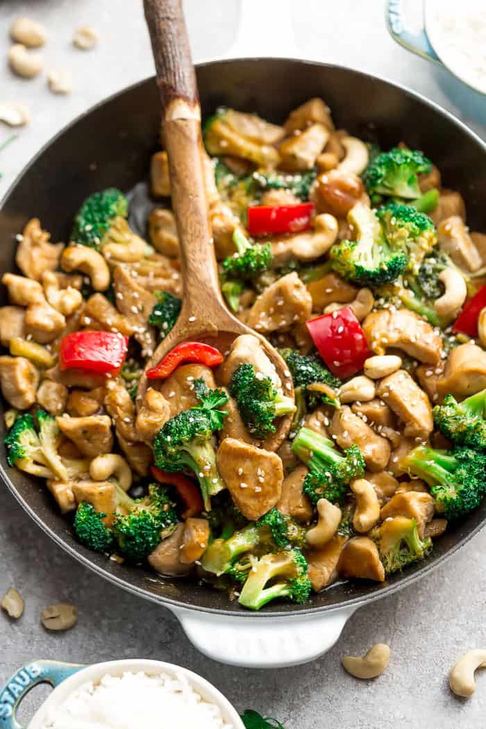 A close-up shot of a skillet full of cashew chicken with a wooden spoon scooping out a spoonful