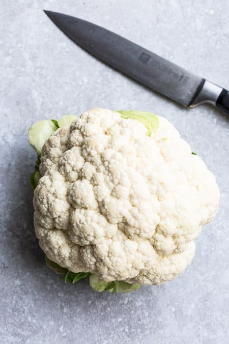 Close-up view of cauliflower head on a grey background with a knife