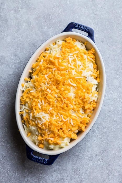 Top view of unbaked caulfilower casserole with cheddar cheese in a pan on a grey background