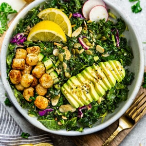 Overhead view of one serving of gnocchi salad, with kale, avocado and lemon in a white bowl with a gold fork on the side