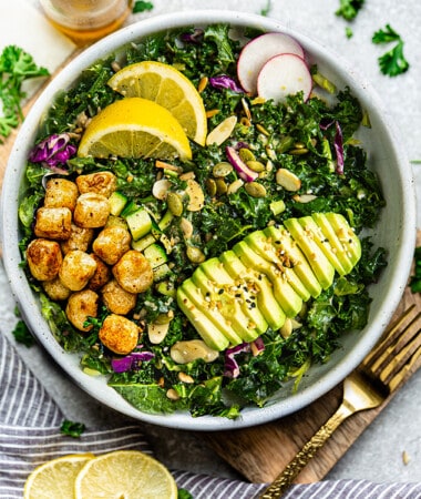 Overhead view of one serving of gnocchi salad, with kale, avocado and lemon in a white bowl with a gold fork on the side