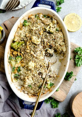 Top view of cauliflower gratin in a blue oval casserole dish on a wooden board with a golden spoon