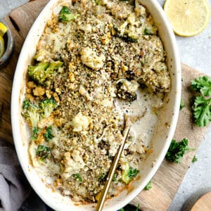 Top view of cauliflower gratin in a blue oval casserole dish on a wooden board with a golden spoon